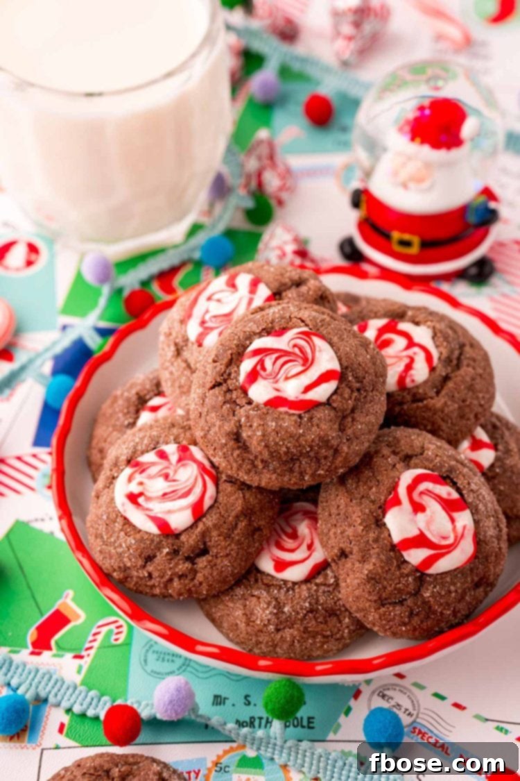 Mint Chocolate Thumbprint Treasures 2 Close up photo of a small plate filled with chocolate peppermint thumbprint cookies. Holiday decor and a glass of milk are around the plate.