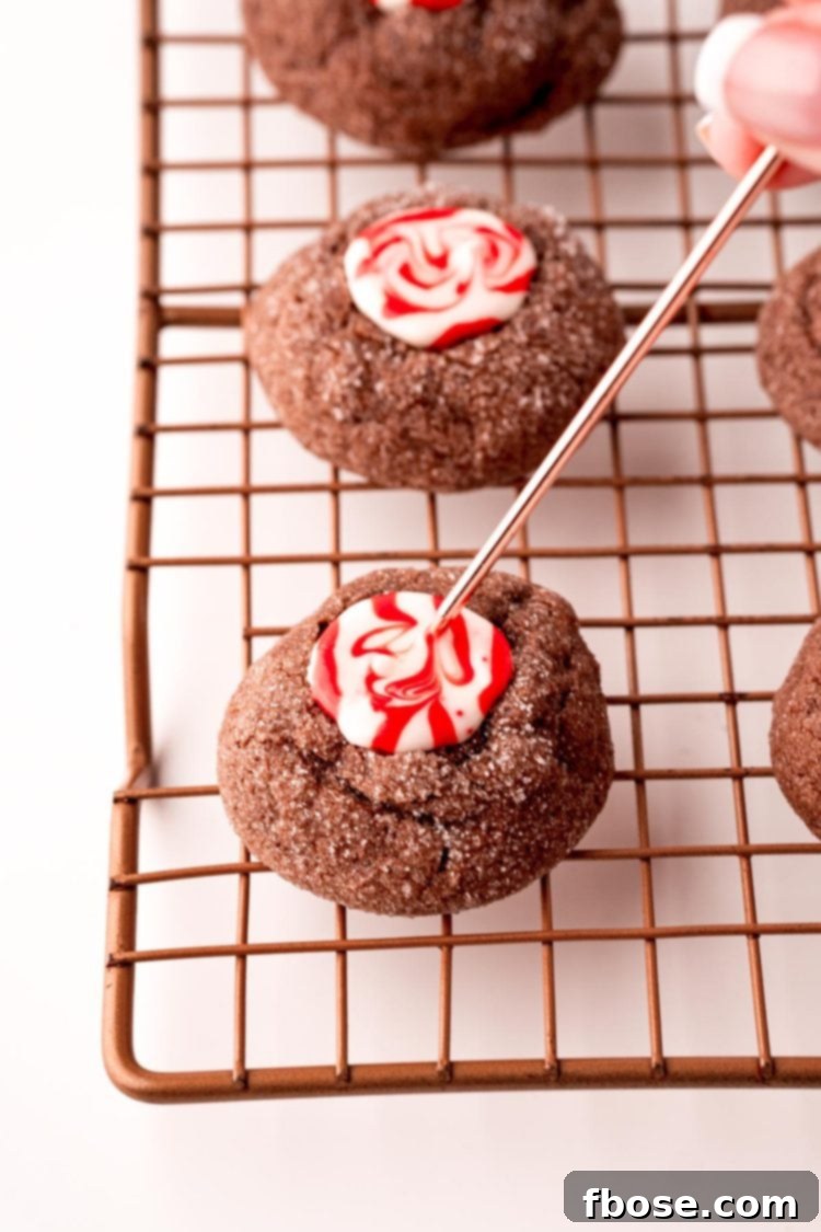 Mint Chocolate Thumbprint Treasures 8 Chocolate thumbprint cookies on a wire rack with a woman's hand swirling the melted candy with a toothpick.