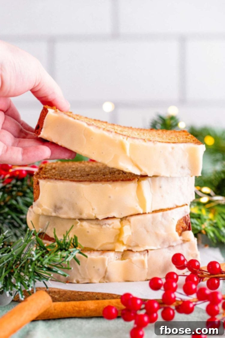 Close up photo of a stack of eggnog bread slices, a woman's hand is taking the top slice off. Holiday decor surrounds the bread.