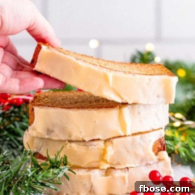 Close up photo of a stack of eggnog bread slices, a woman's hand is taking the top slice off. Holiday decor surrounds the bread.