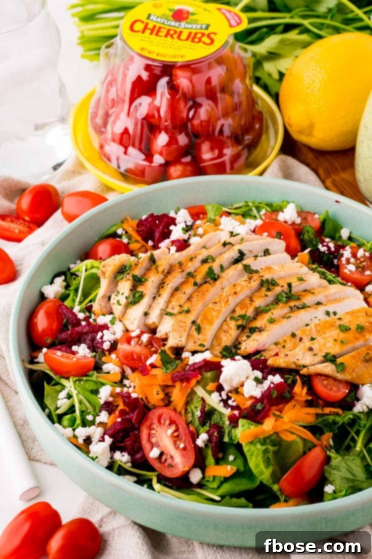 Close up photo of a grilled chicken salad with beets, tomatoes, greens, and goat cheese.