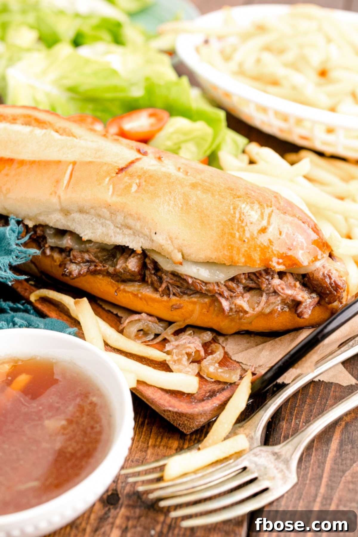 Close up photo of French Dip sandwiches on a wooden board with French fries, showcasing the tender beef and melted cheese.