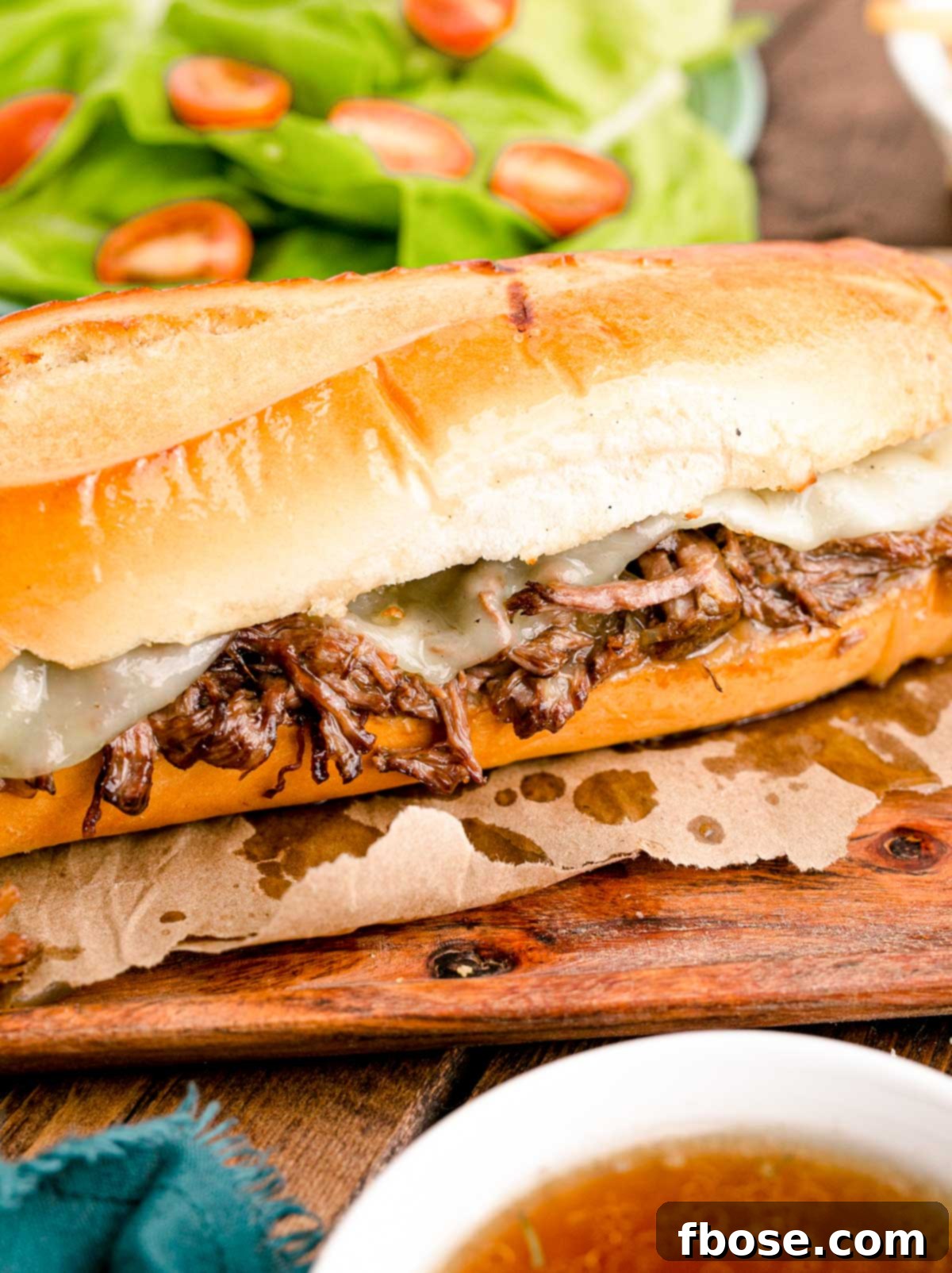 Close up photo of French Dip sandwiches on a wooden board with French fries, ready to be enjoyed.