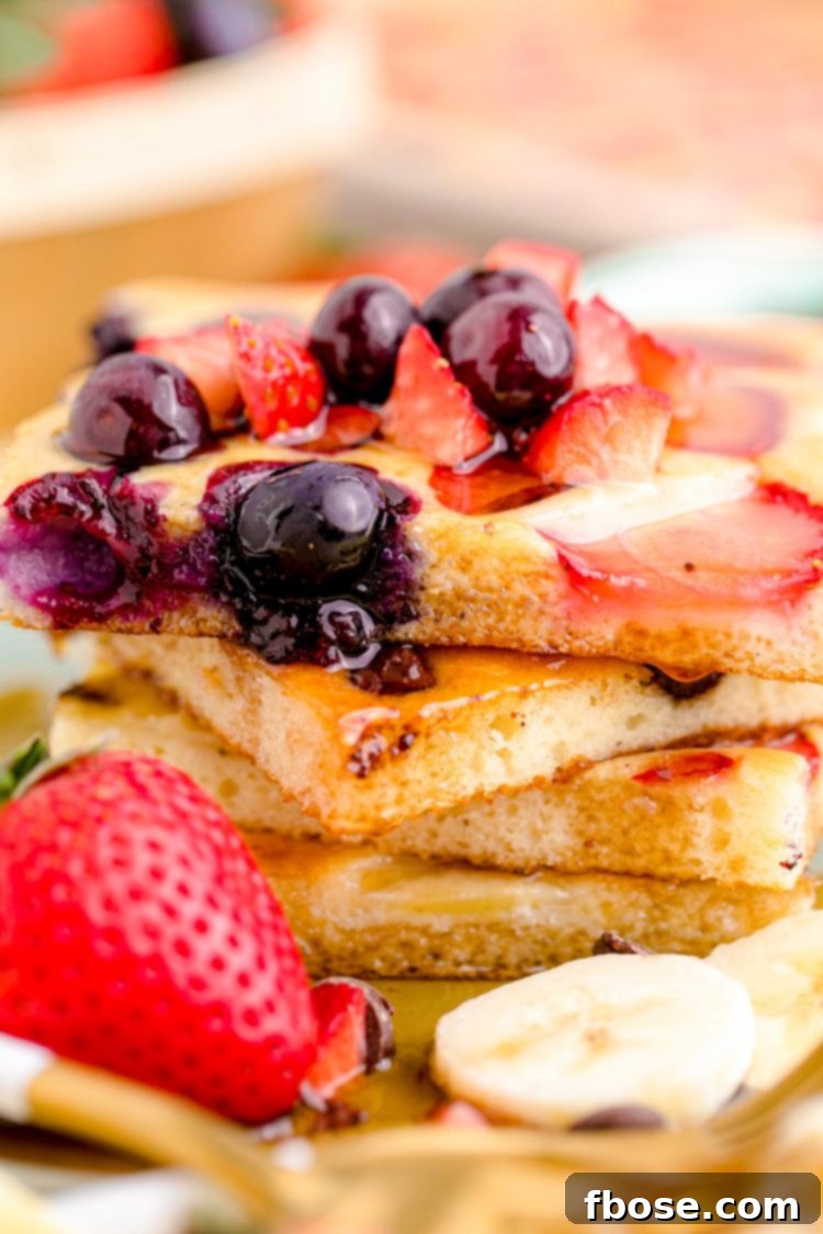 Close-up of fluffy sheet pan pancakes on a plate, garnished with fresh berries and a drizzle of syrup, showcasing the golden-brown edges and soft interior.