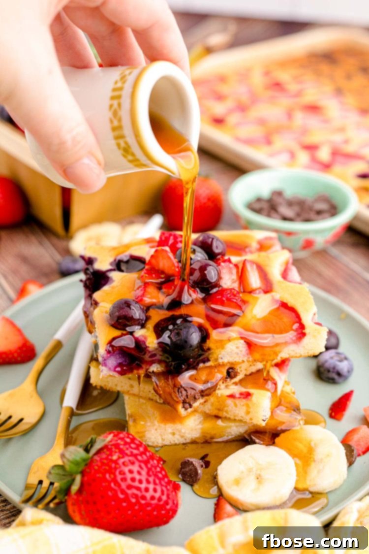 A hand pouring warm maple syrup generously over a freshly baked slice of sheet pan pancake, highlighting the golden color and inviting texture.