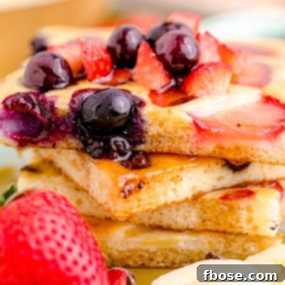 Close up photo of a stack of sheetpan pancakes on a plate with fruit around it.