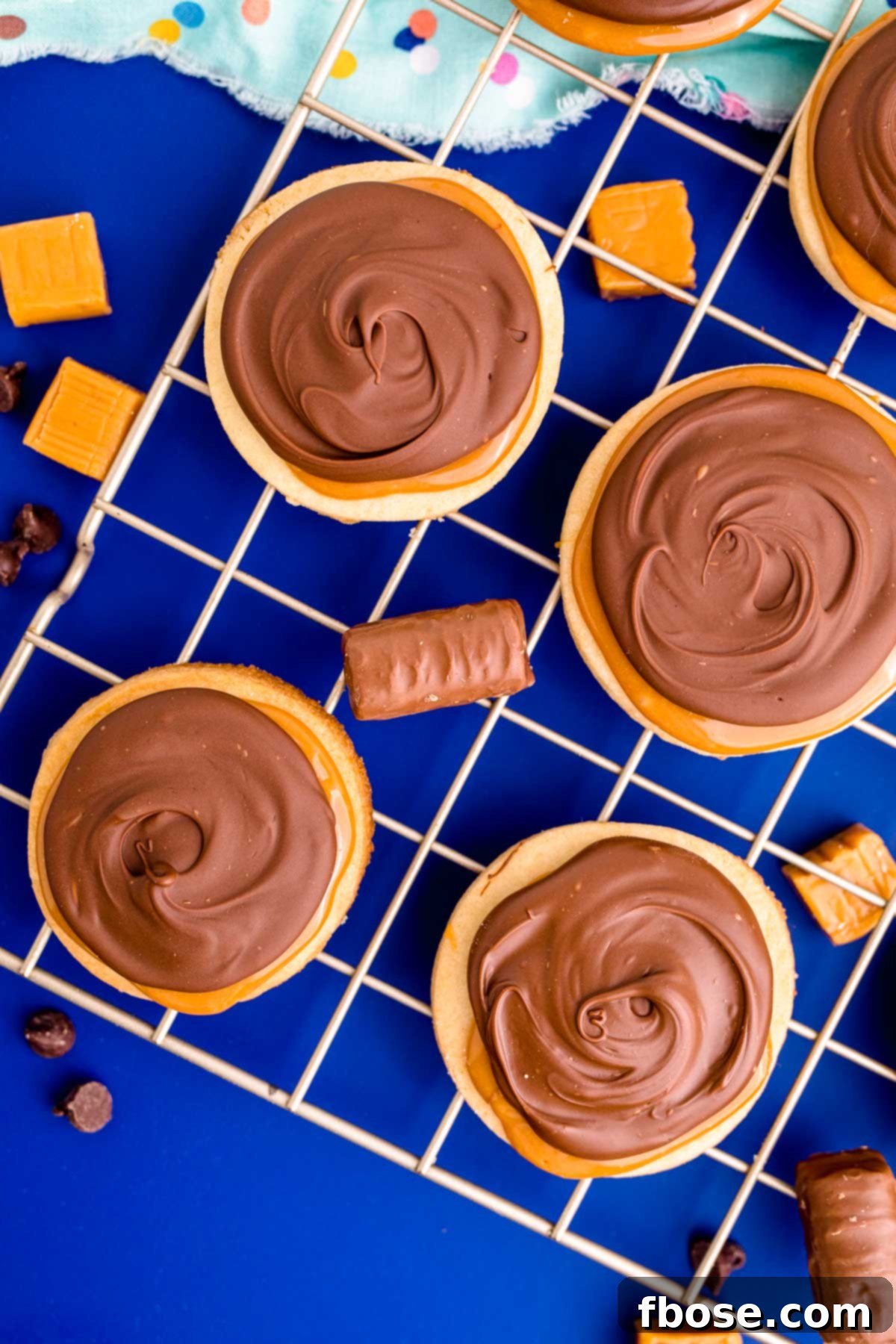 Overhead photo of Twix cookies cooling on a wire rack on a blue surface, showing their perfectly set layers.