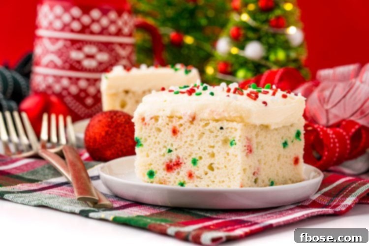 Yuletide Delight 3 A slice of funfetti Christmas cake on a white plate on a holiday napkin with decor in the background.