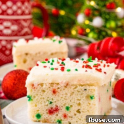A slice of funfetti Christmas cake on a white plate on a holiday napkin with decor in the background.