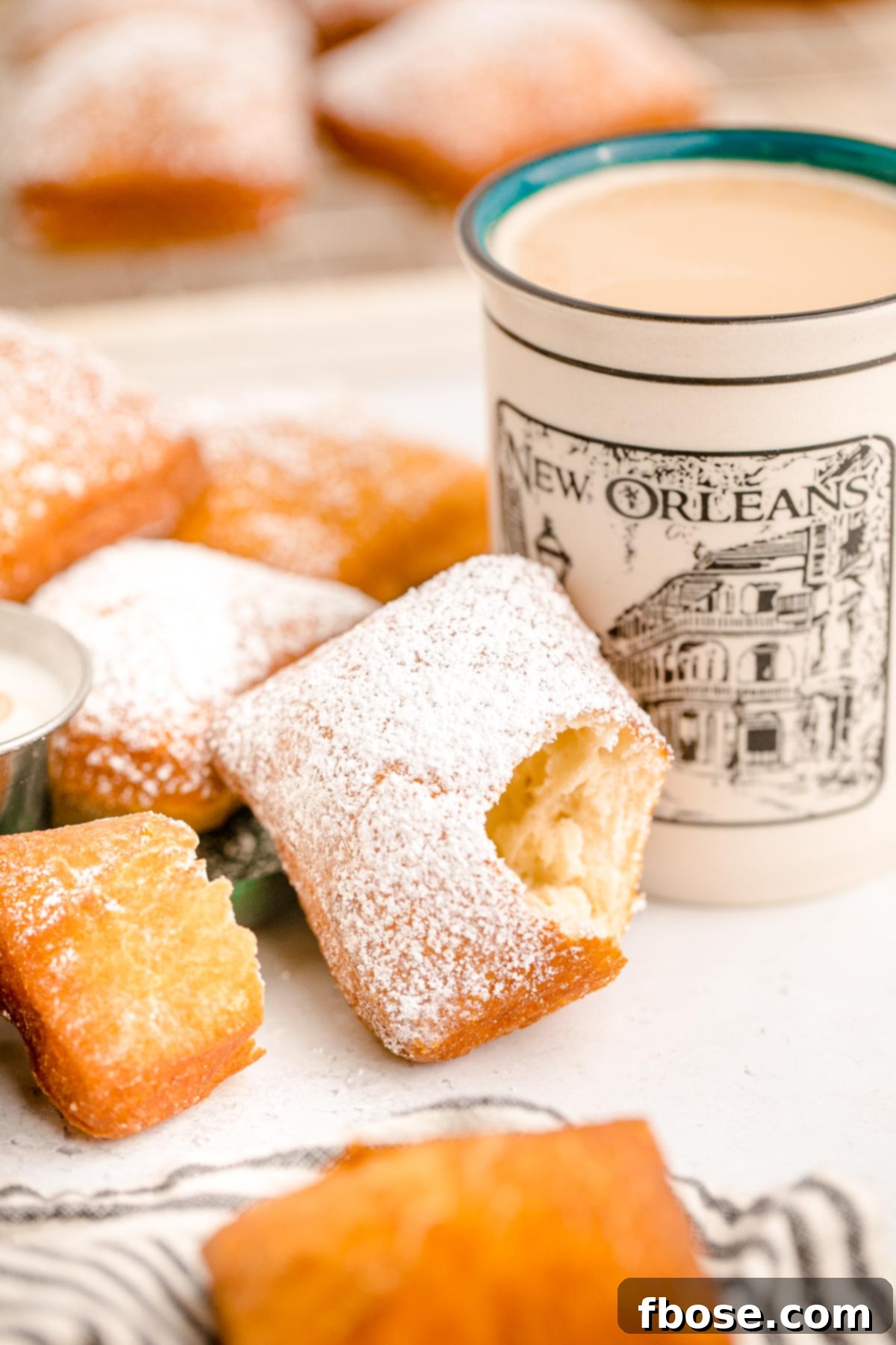 A Beignets covered in powdered sugar leaning on a mug of coffee with a bite taken out of it.