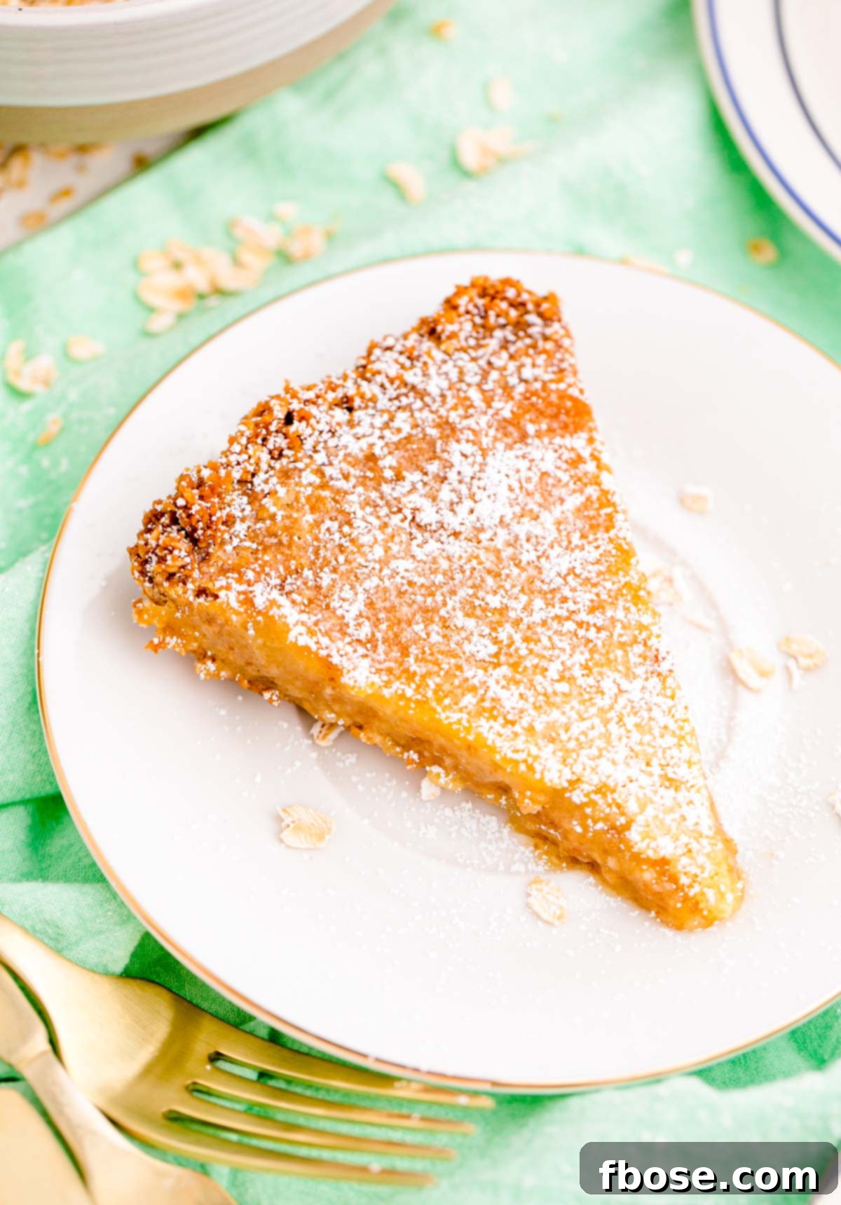 Close up photo of a slice of Milk Bar Pie on a white plate on a green napkin, showcasing its gooey filling and rustic crust.