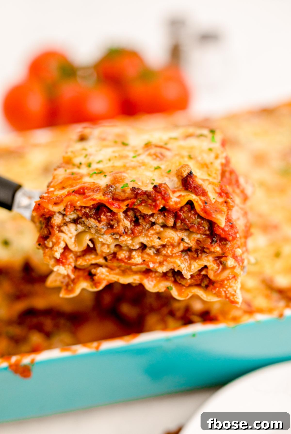 Close up photo of a spatula pulling a slice of lasagna from a teal casserole dish.