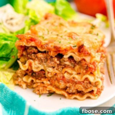 A slice of lasagna on a white plate with a salad.