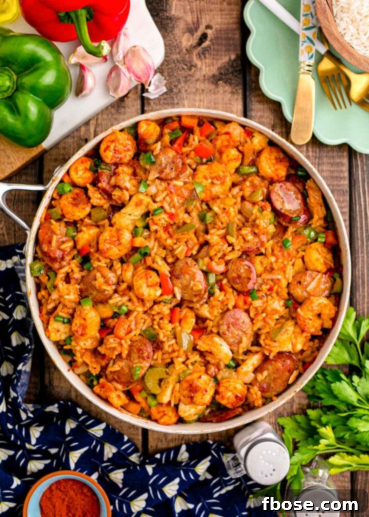 Overhead photo of a pan of jambalaya on a wooden table with a navy napkin and ingredients around it.