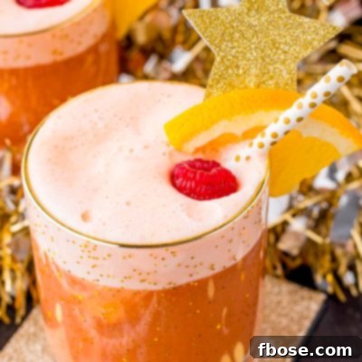 A close up photo of party punch garnished with a raspberry and orange slice on a gold coaster with party decorations in the background.