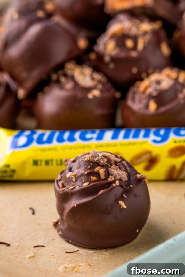 Butterfinger truffles delicately arranged on parchment paper, with more in the background, showing off their crunchy exterior.