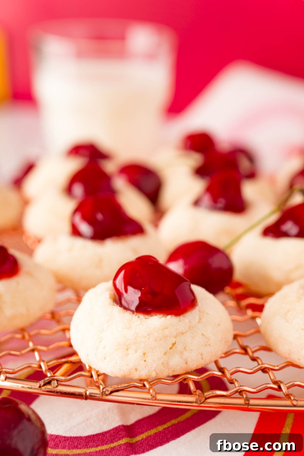 Close-up photo of cherry cookies cooling on a copper wire rack, with more finished cookies visible in the background.
