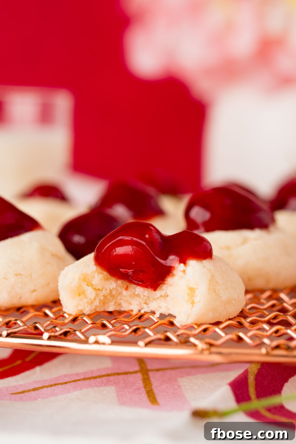 Close-up photo of a cherry cheesecake cookie with a bite taken out, resting on a copper wire rack.