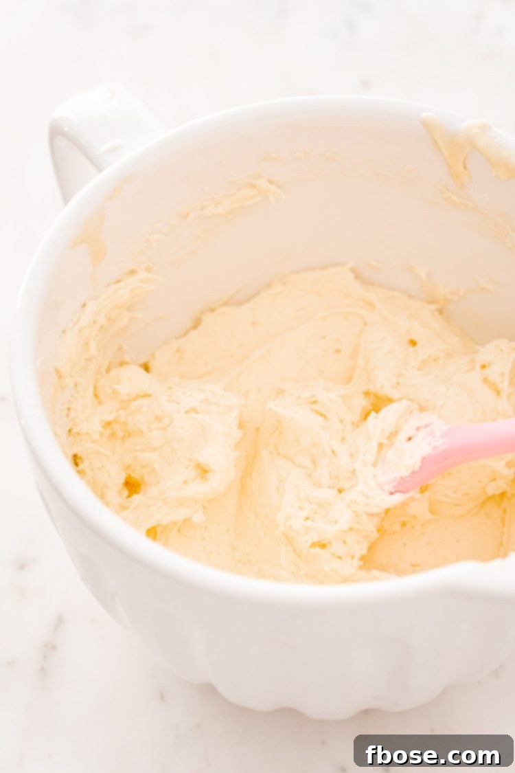 A pristine white mixing bowl showcases the smooth, creamy consistency of the cheesecake base ingredients—cream cheese and powdered sugar—being expertly blended together.