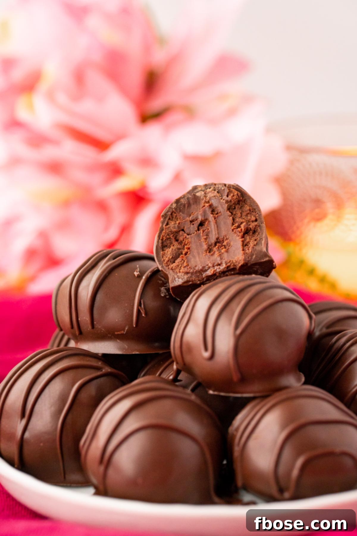 The Ultimate Chocolate Truffles Recipe 2 Close up photo of chocolate truffles stacked on a white plate on a pink napkin.
