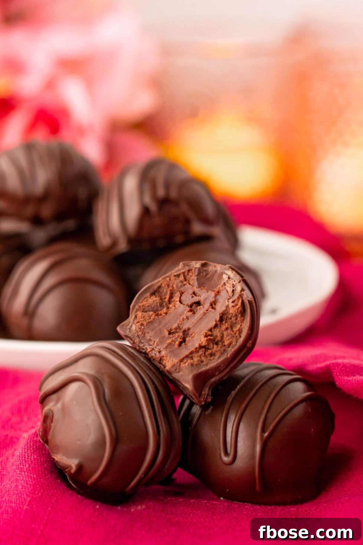 The Ultimate Chocolate Truffles Recipe 3 Close up photo of three chocolate truffles on a pink napkin with a bite taken out of the top one.