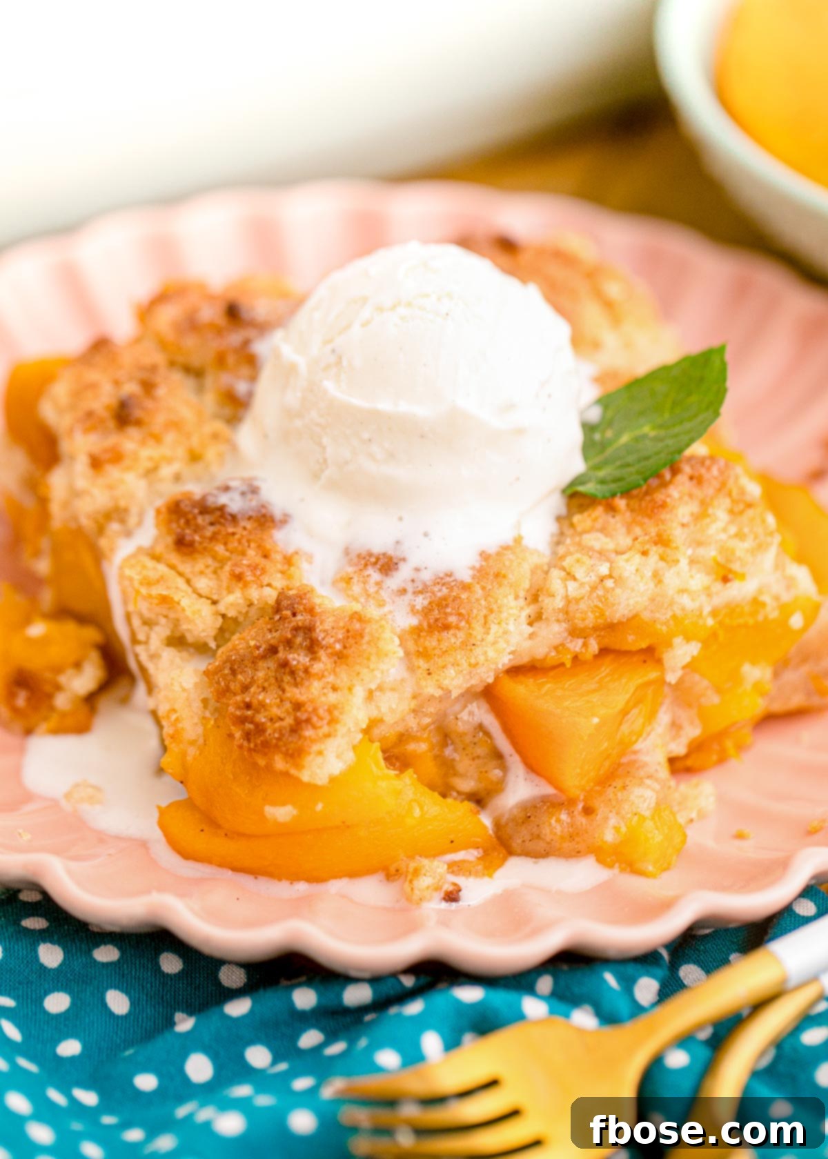 Close up photo of a slice of peach cobbler on a pink plate on a blue napkin.