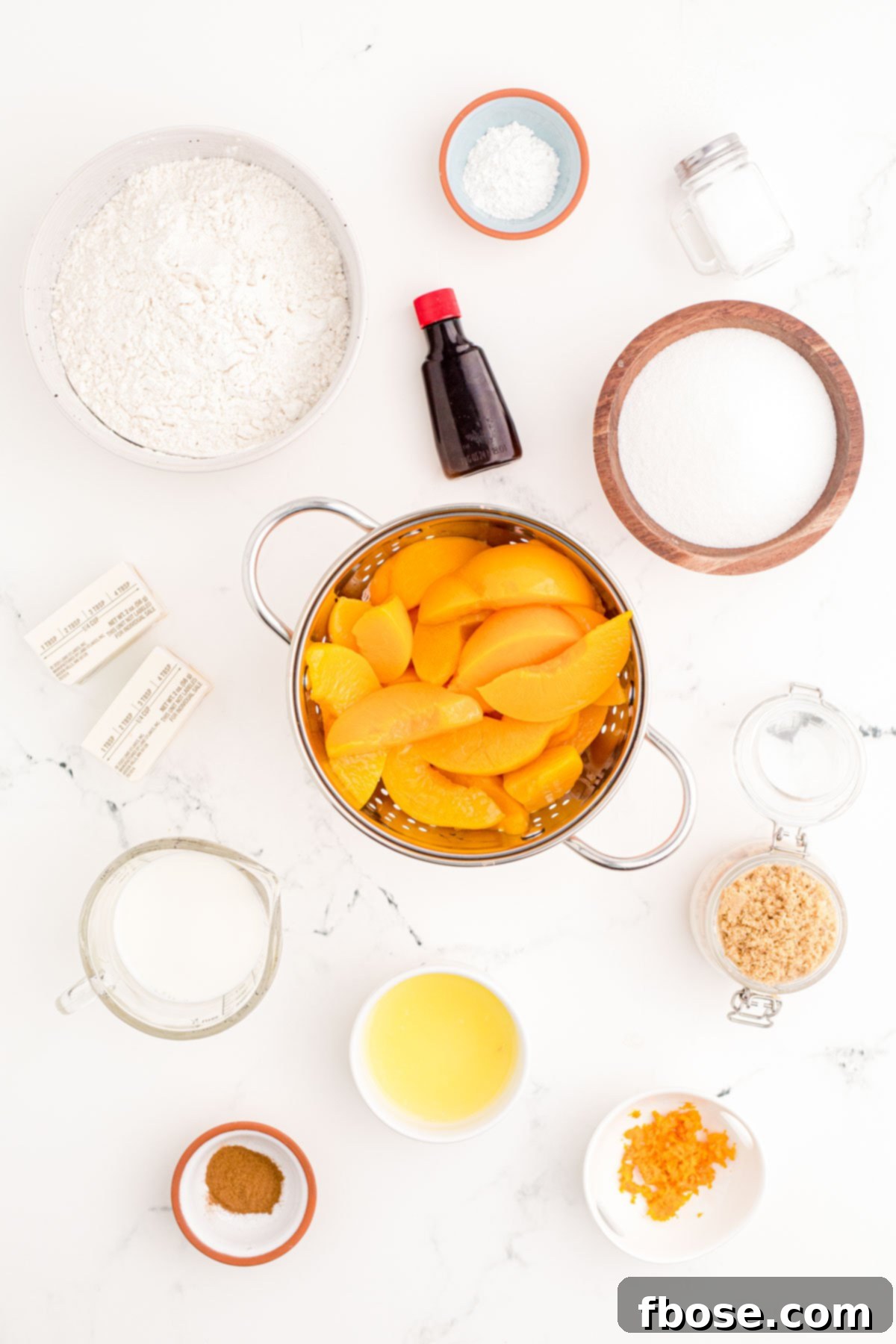 Ingredients to make peach cobbler prepped on a marble counter.
