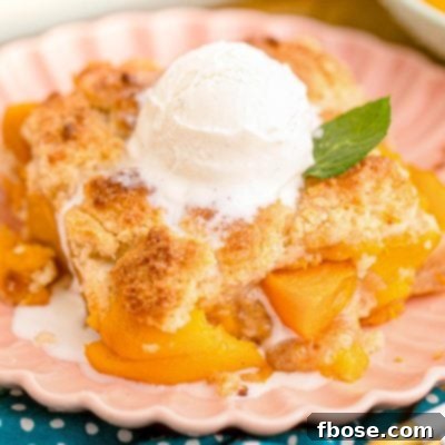 Close up photo of a slice of peach cobbler on a pink plate on a blue napkin.