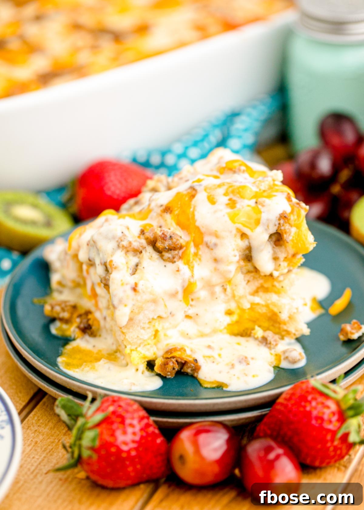 A slice of biscuits and gravy casserole on a blue plate surrounded by berries.