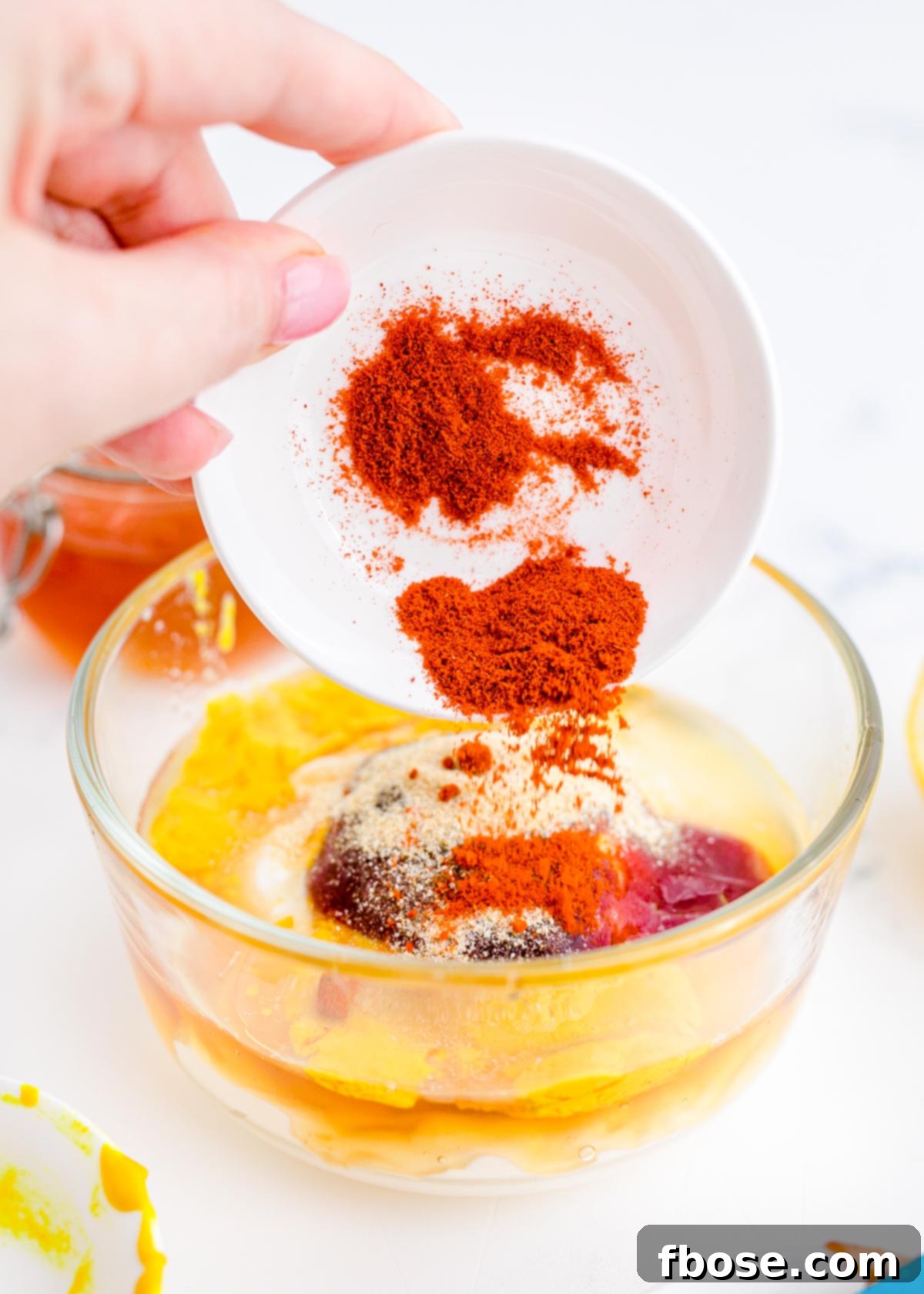 A woman's hand adding a pinch of spices into a bowl of creamy yellow sauce to make a dipping sauce.