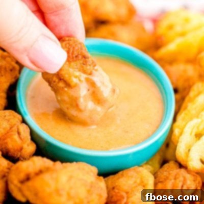 Close up photo of a woman's hand dipping a chick fil a nugget into homemade chick fil a sauce in a teal bowl.