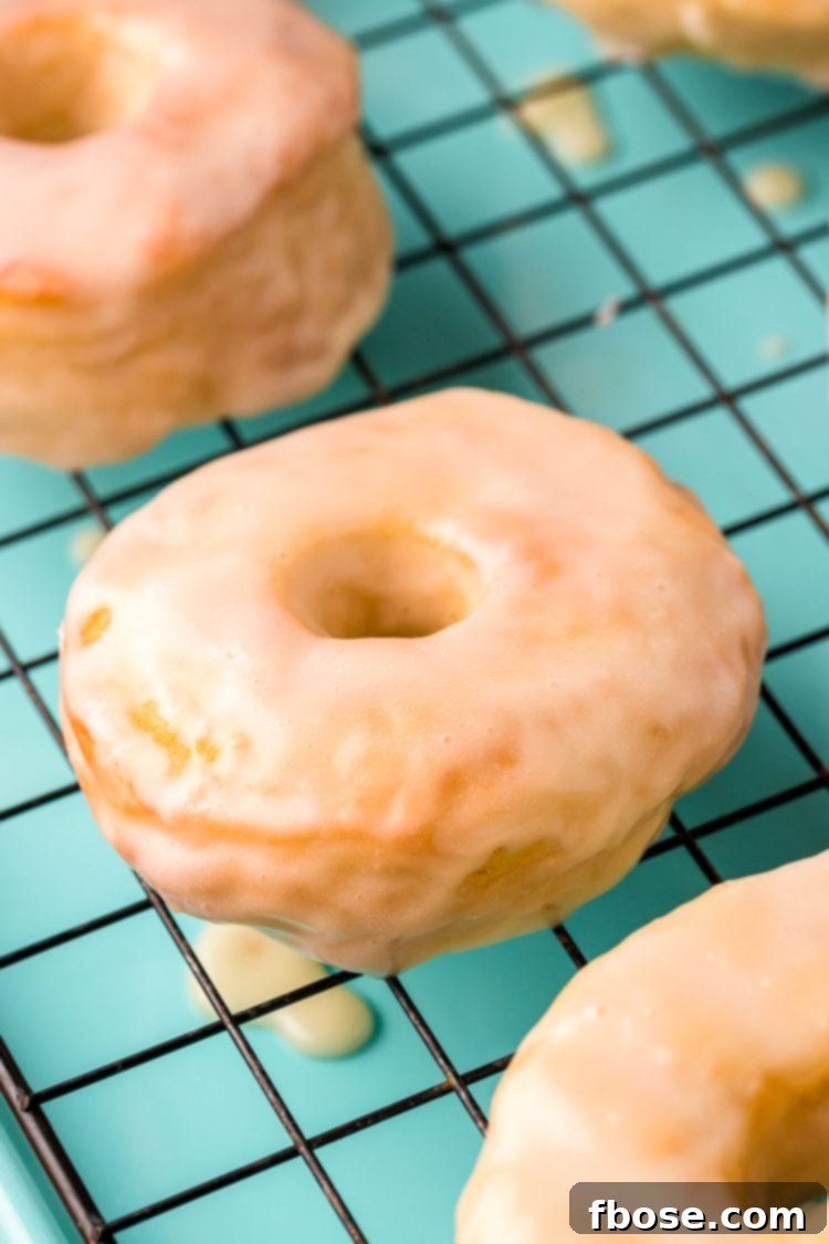 Close up photo of glazed donuts cooling on a wire rack on a teal baking sheet.