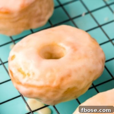 Close up photo of glazed donuts cooling on a wire rack on a teal baking sheet.