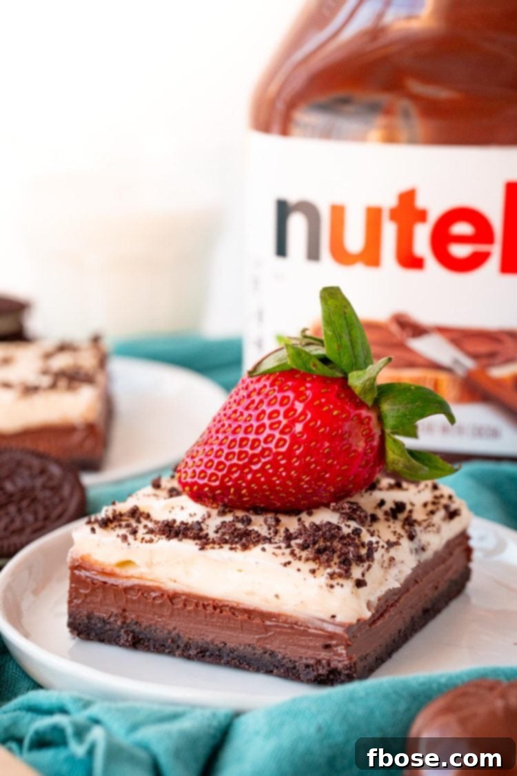 Effortless Nutella Cheesecake Squares 2 Close up photo of a slice of Nutella Cheesecake Bars on a white plate topped with a strawberry on a blue napkin.