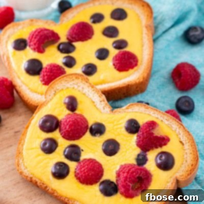 Yogurt Custard Toast 8 Close up photo of two slices of yogurt toast on a wooden cutting board with a blue napkin and berries around it.