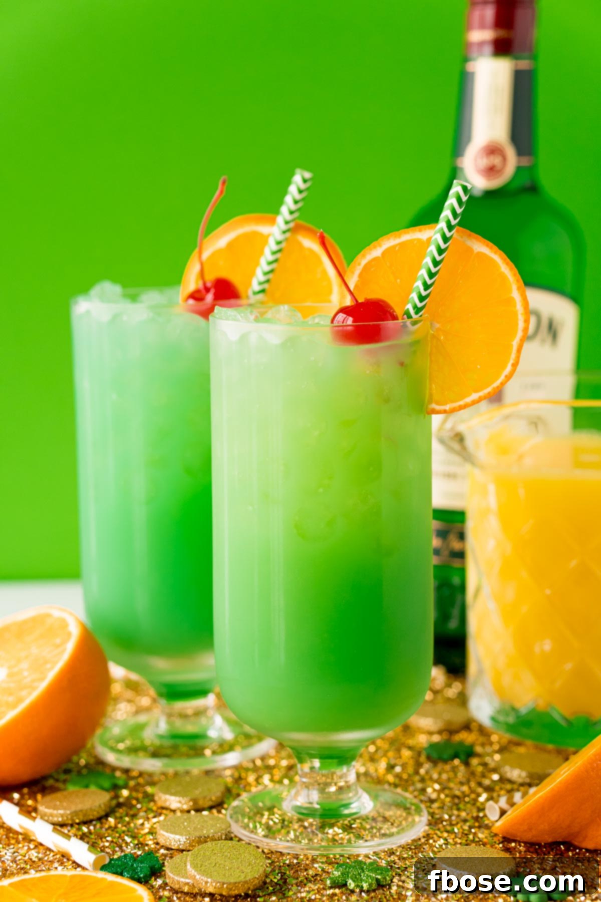 Jig Juice 3 Two green drunken leprechaun cocktails on a gold placemat with oranges and Jameson in the background.