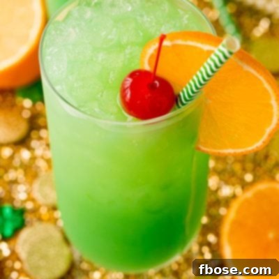 Jig Juice 9 Highball glass filled with a green cocktail garnished with orange slice and maraschino cherry.
