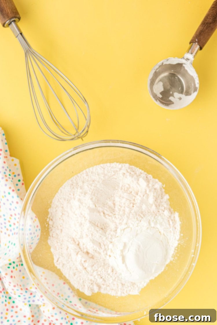 All-purpose flour and cornstarch being gently combined in a clear glass mixing bowl with a whisk.