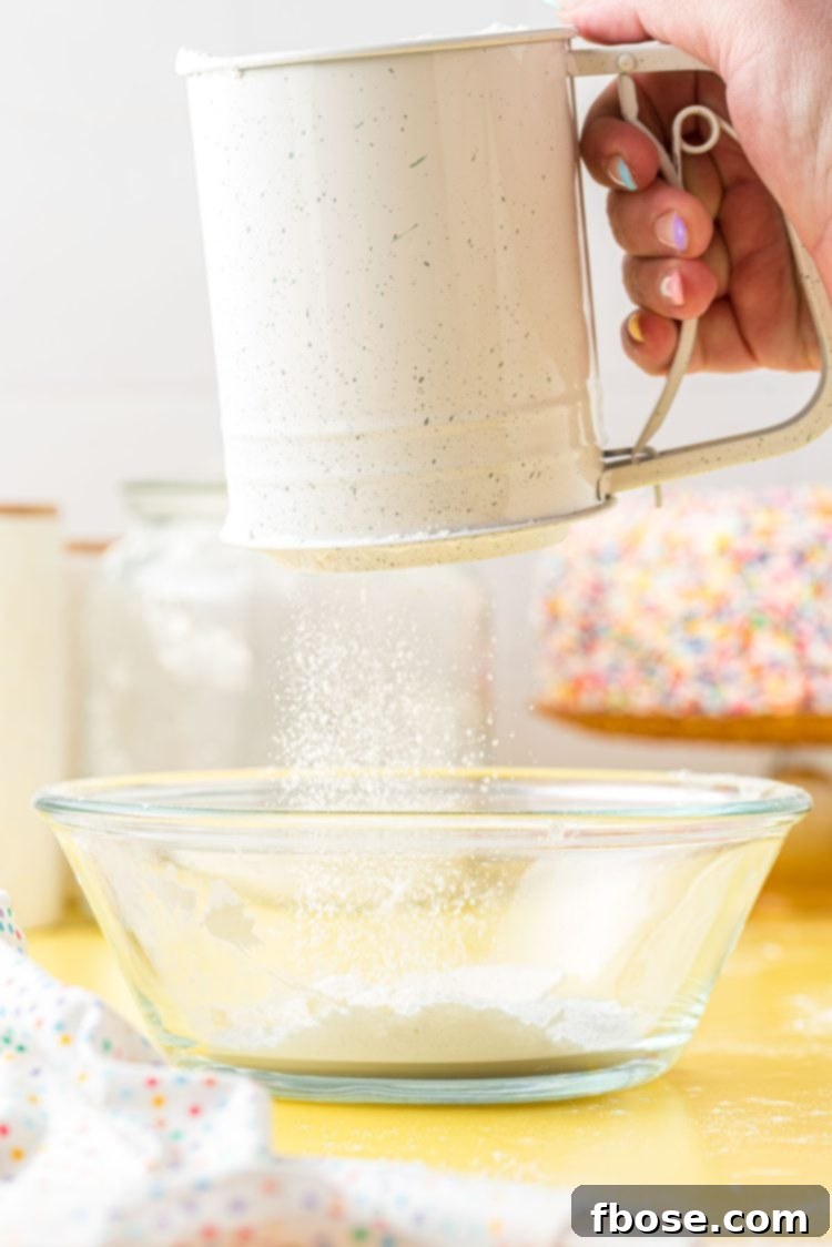 Homemade cake flour substitute being meticulously sifted into a clean glass mixing bowl, demonstrating the crucial aeration process.