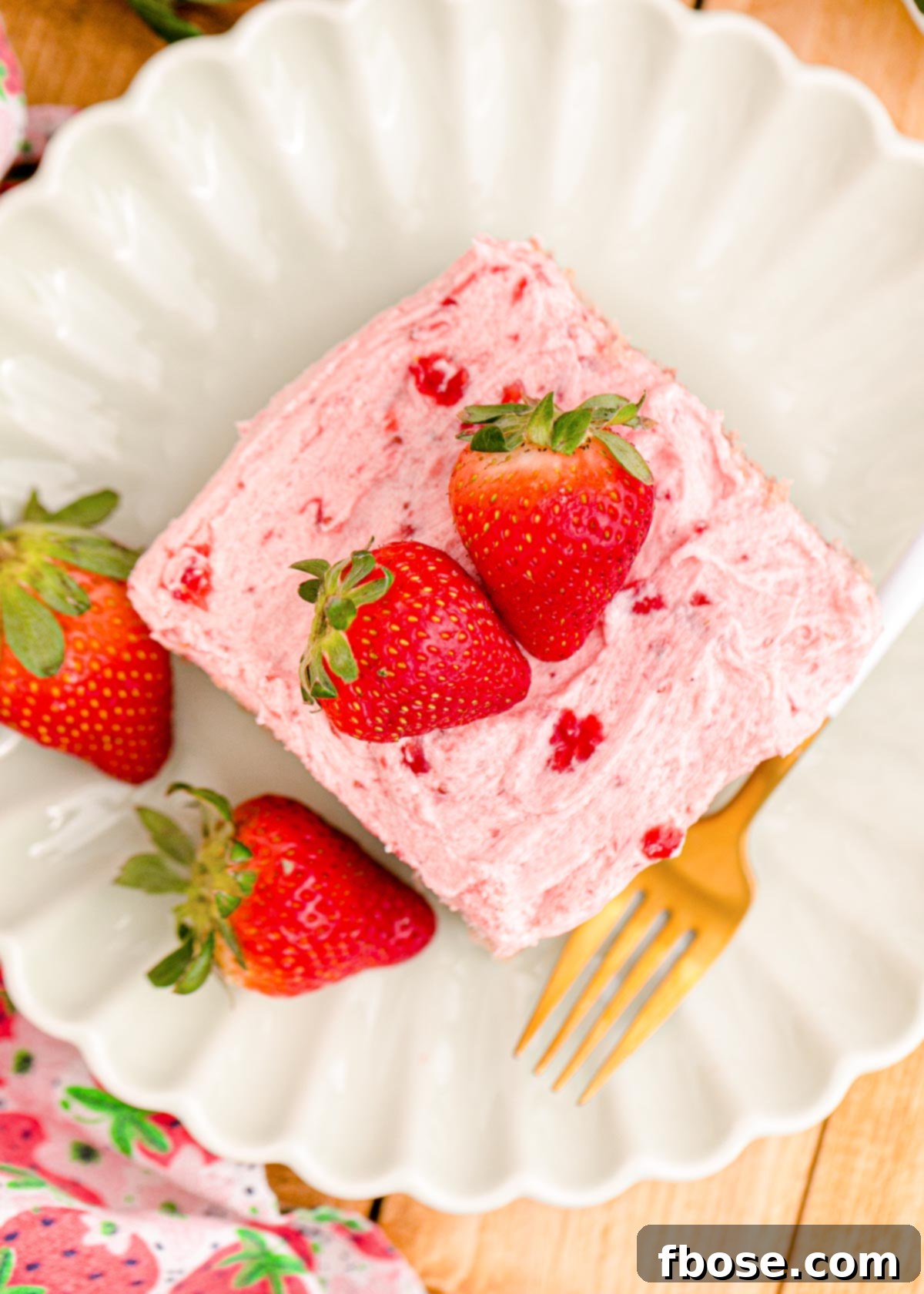 Overhead photo of strawberry sheet cake on a white scalloped plate.