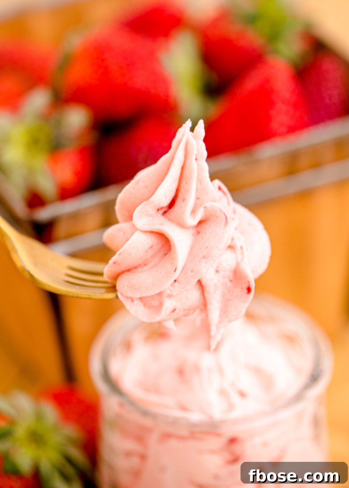 A fork lifting a bite of strawberry buttercream frosting out of a bowl.