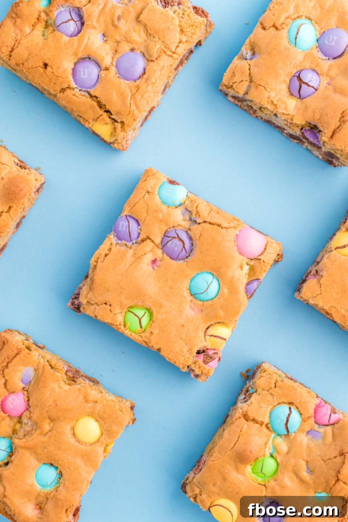 A generous tray of freshly baked Easter blondies, studded with colorful M&M candies, arranged on a vibrant blue surface, ready to be served.