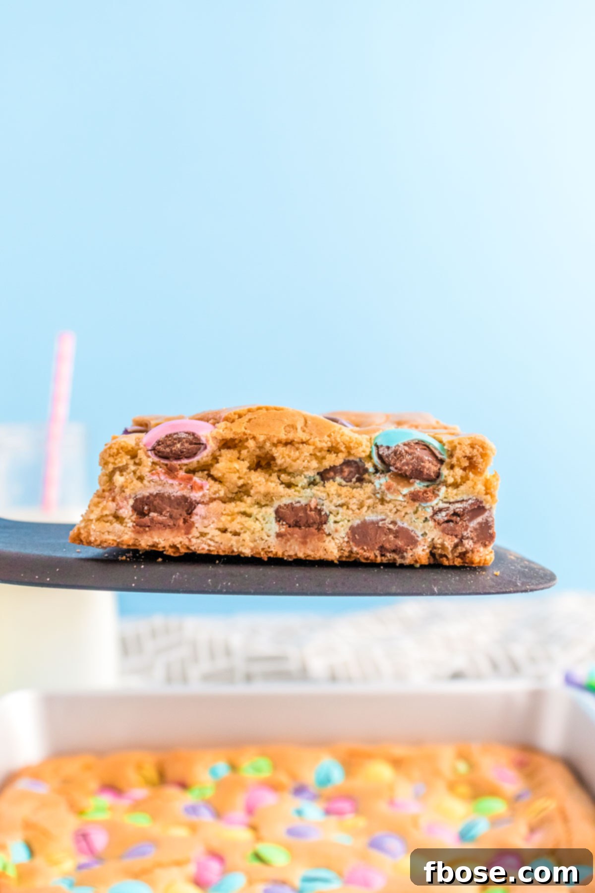 A spatula gently lifting a perfect slice of Easter blondie bar, rich with colorful M&Ms, from a baking pan.