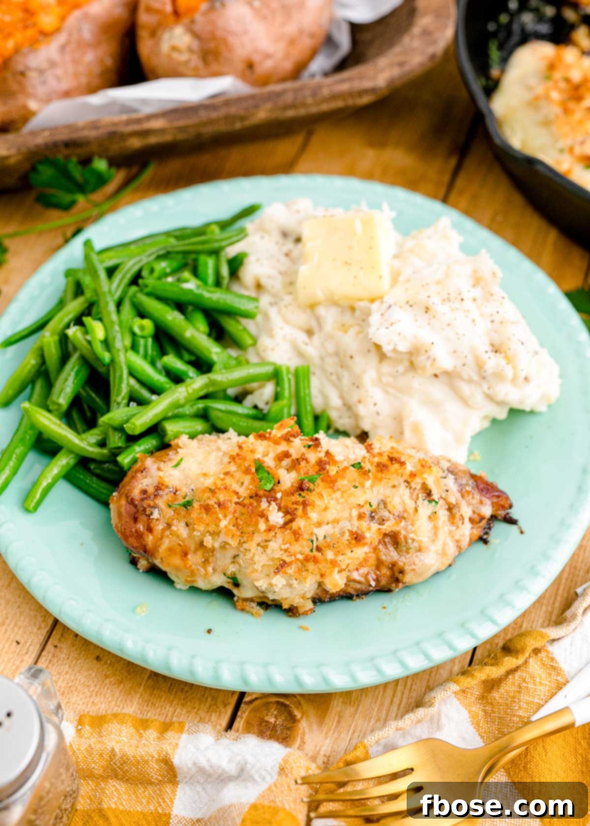 Parmesan crusted chicken on a blue plate with mashed potatoes and green beans.