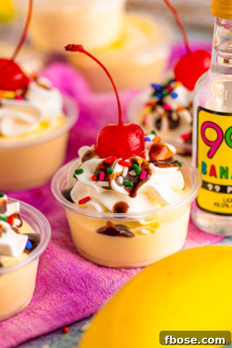 Close up photo of banana split pudding shots in plastic shot containers, topped with whipped cream, chocolate syrup, and a cherry.