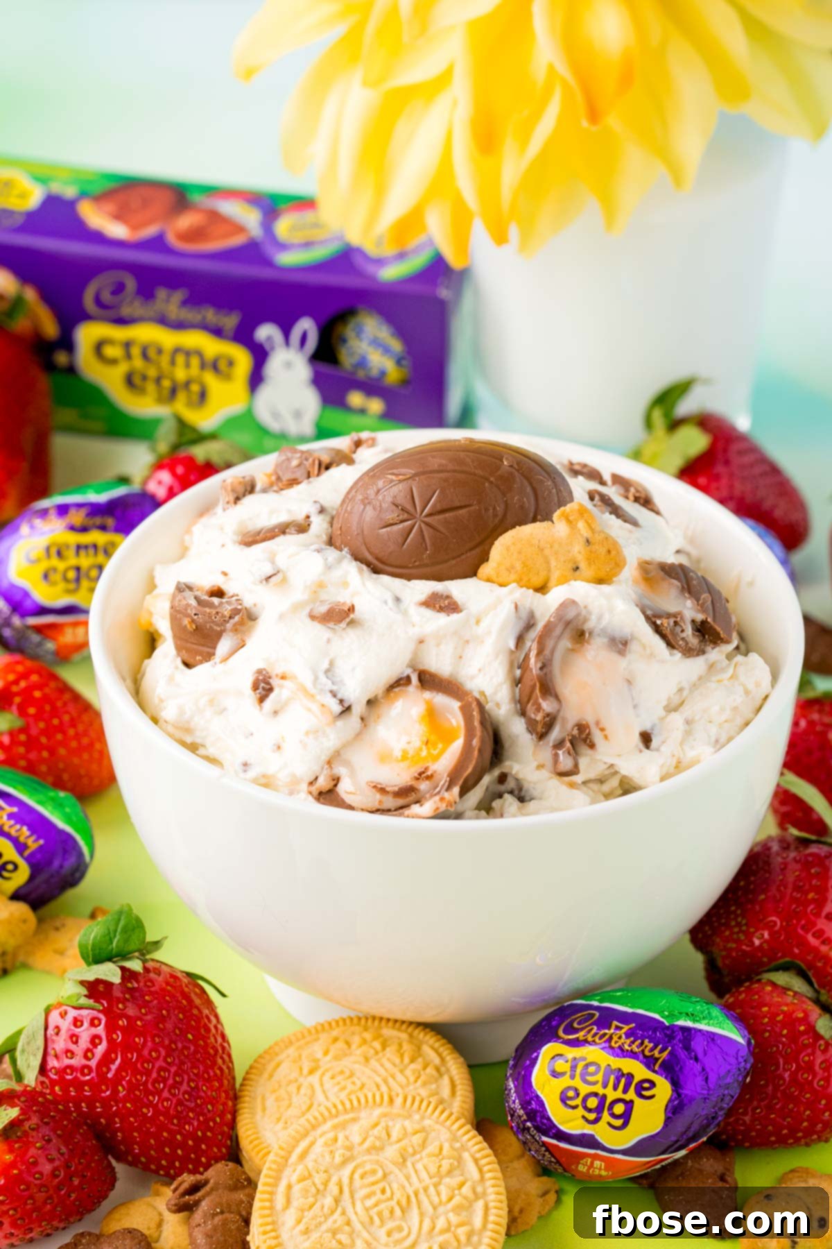 A white bowl with cadbury creme egg dip in it with strawberries around it, ready for serving.