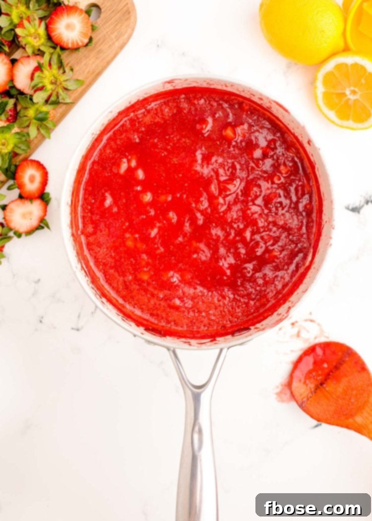 Smooth, glossy strawberry puree cooling in a stainless steel pot after cooking.
