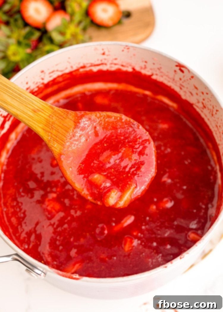 A wooden spoon delicately scooping thick, red strawberry puree from a pot.