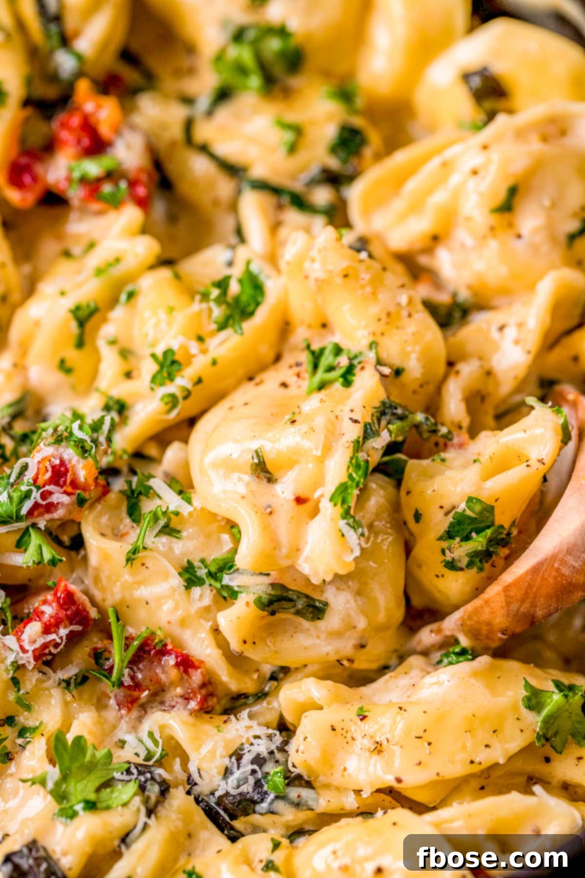Close up photo of a wooden spoon in a pot of tortellini alla panna, highlighting the creamy texture.