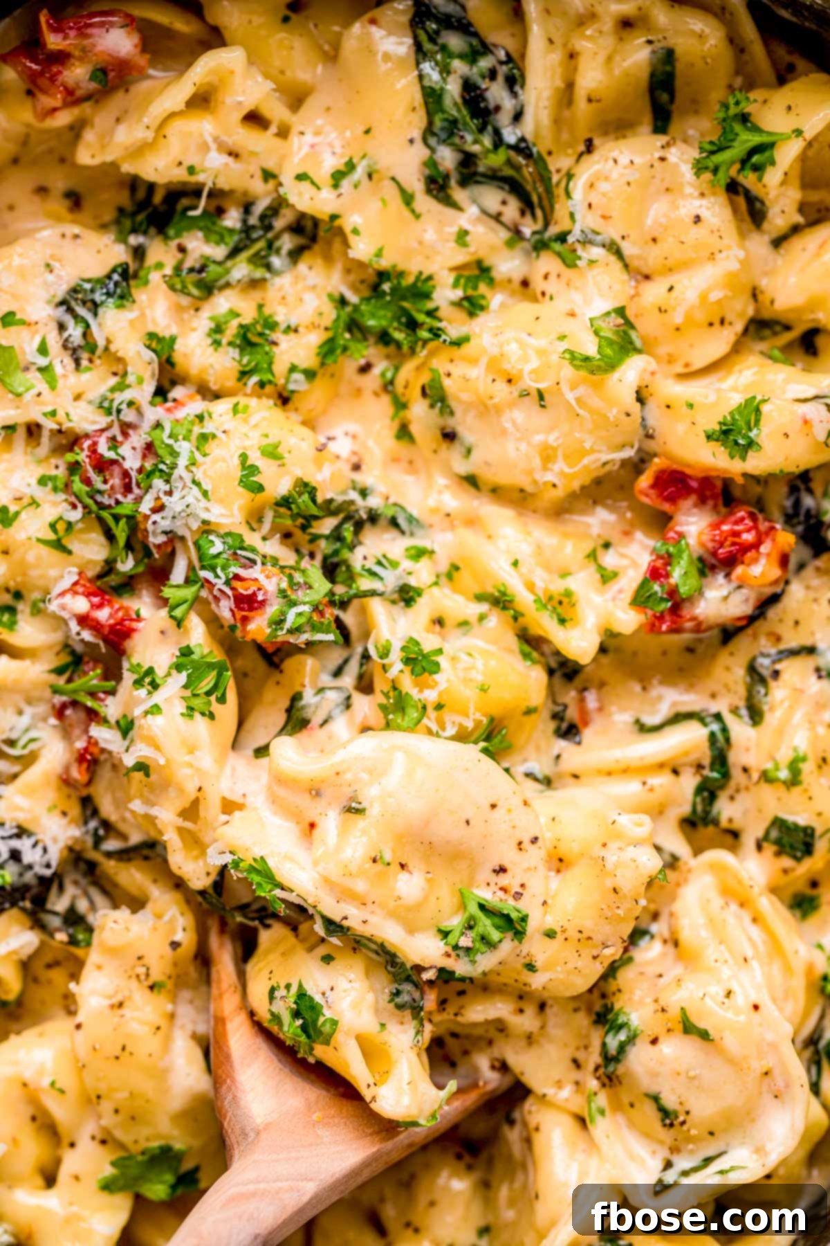 A close-up view of a wooden spoon stirring delicious tortellini alla panna in a pot.